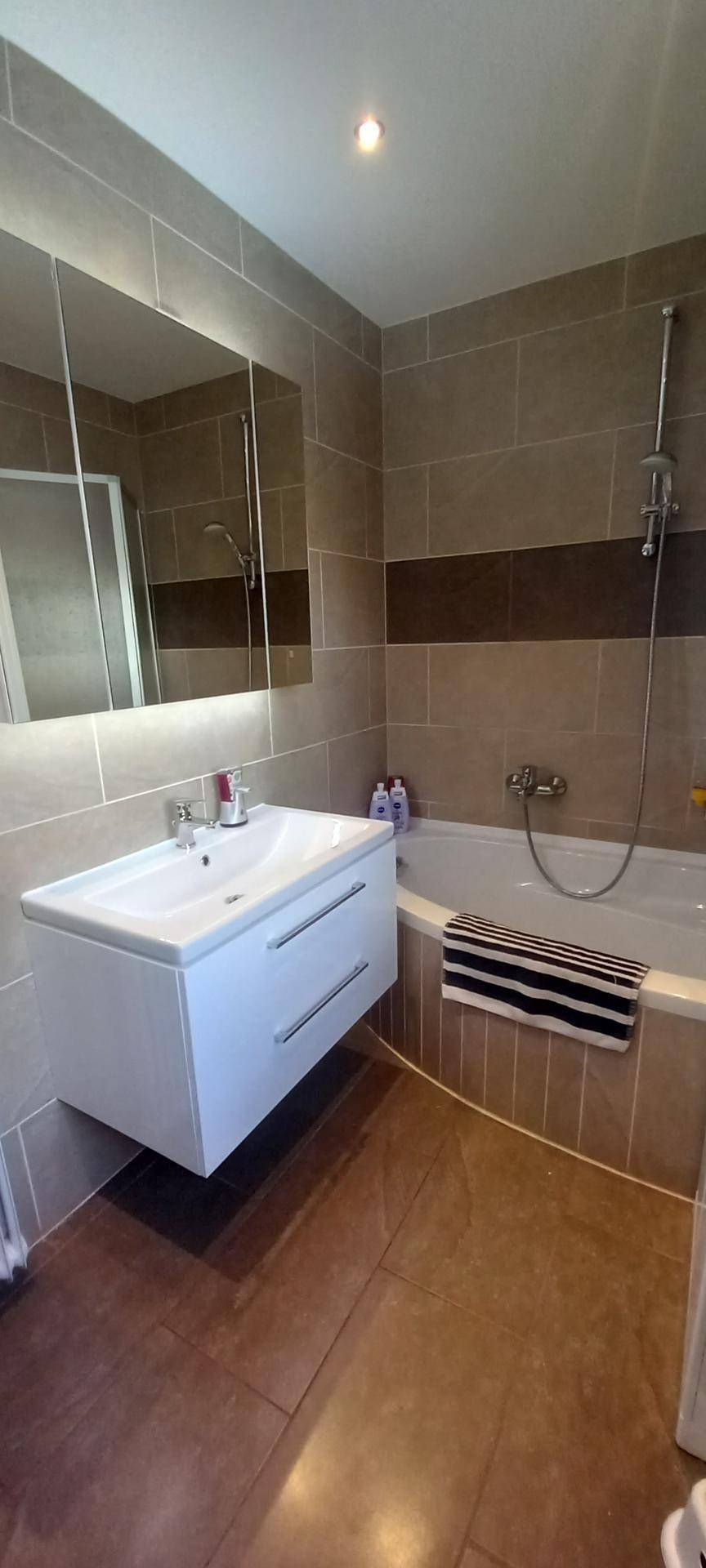 Modernes Badezimmer mit schwebendem Waschtisch, Spiegelschrank und Badewanne mit Duschfunktion.