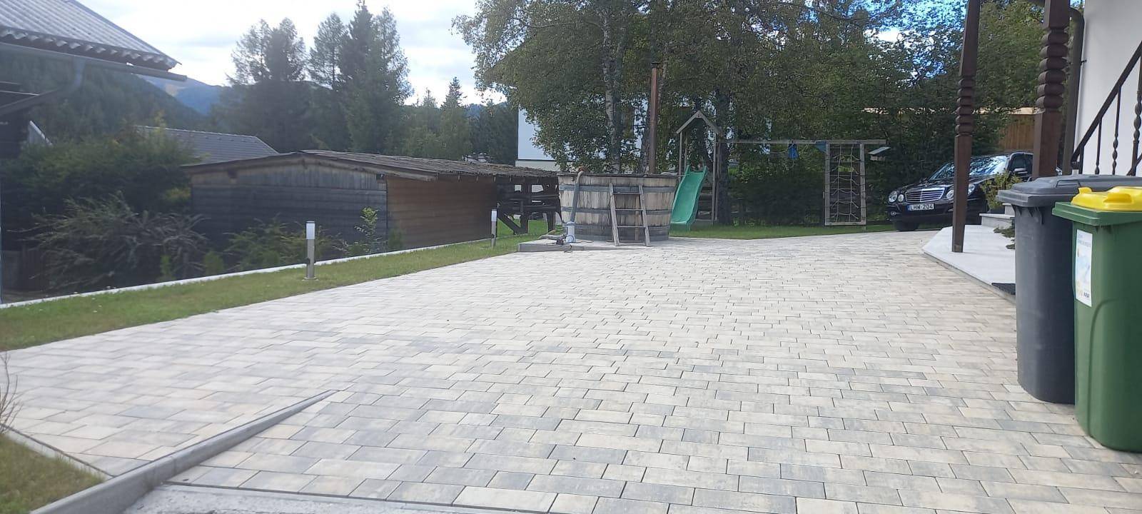 Großer gepflasterter Vorplatz mit Spielplatz im Hintergrund und Mülltonnen am Rand.
