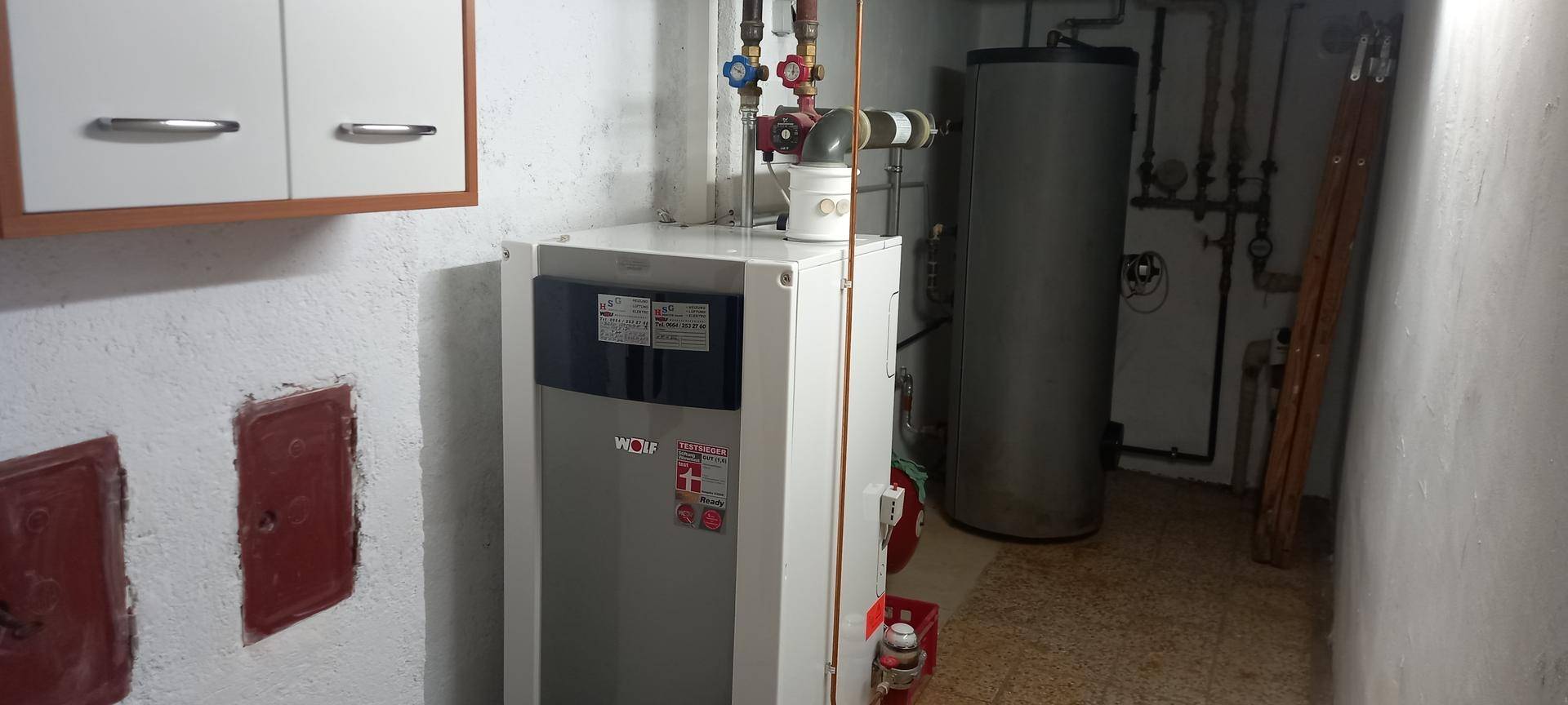 Heizraum mit moderner Heizungsanlage und Warmwasserspeicher in einem Kellerraum.