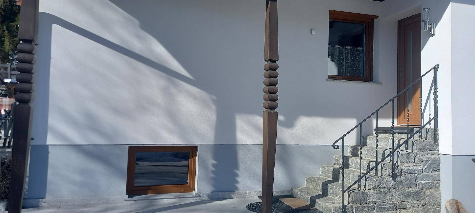Hauseingang mit Steintreppe und schmiedeeisernem Geländer, umgeben von weißer Fassade.