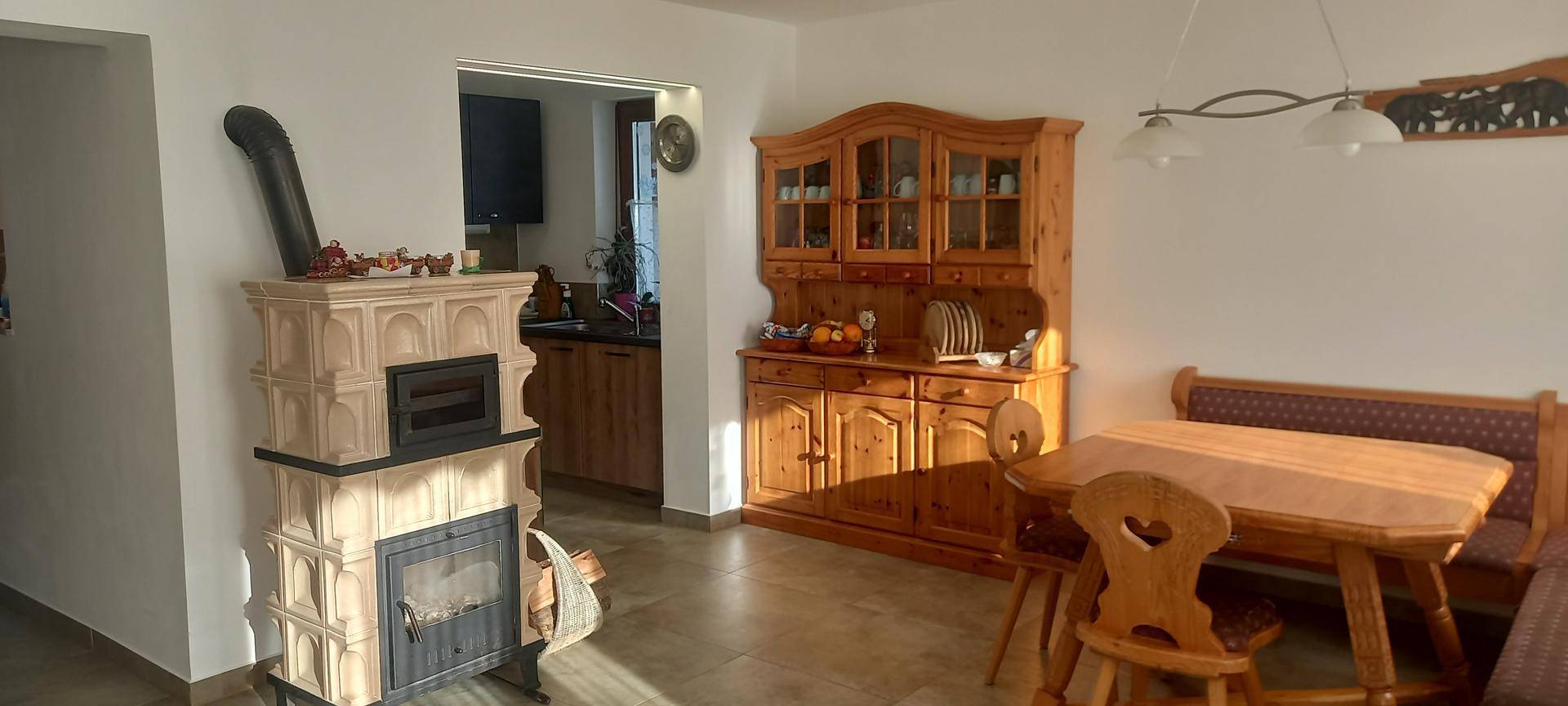 Essbereich mit traditionellem Kachelofen, Holztisch und Schrank, angrenzend an die Küche.