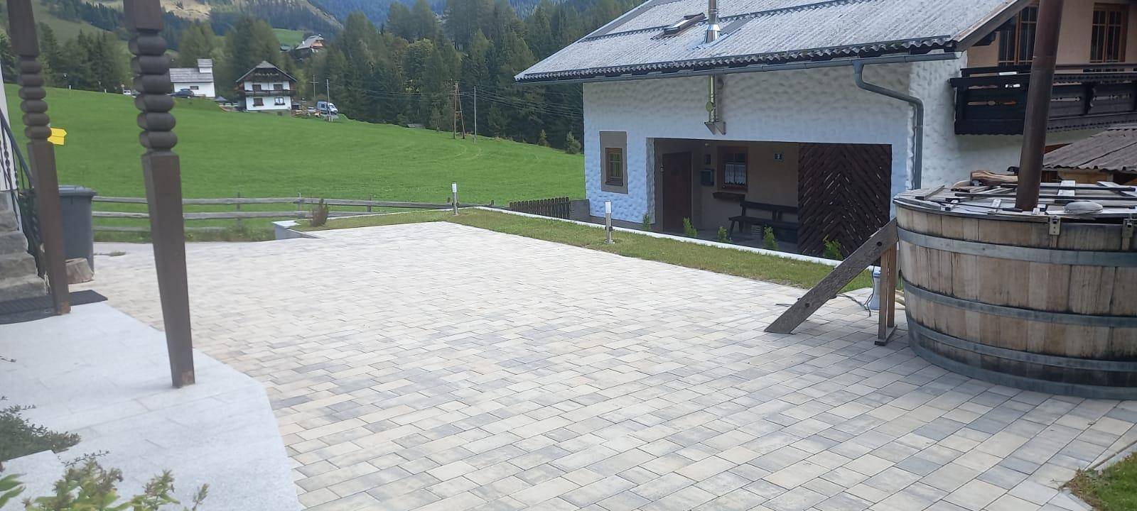 Geräumiger Außenbereich mit gepflasterter Fläche, Rasen und einem hölzernen Whirlpoolfass.