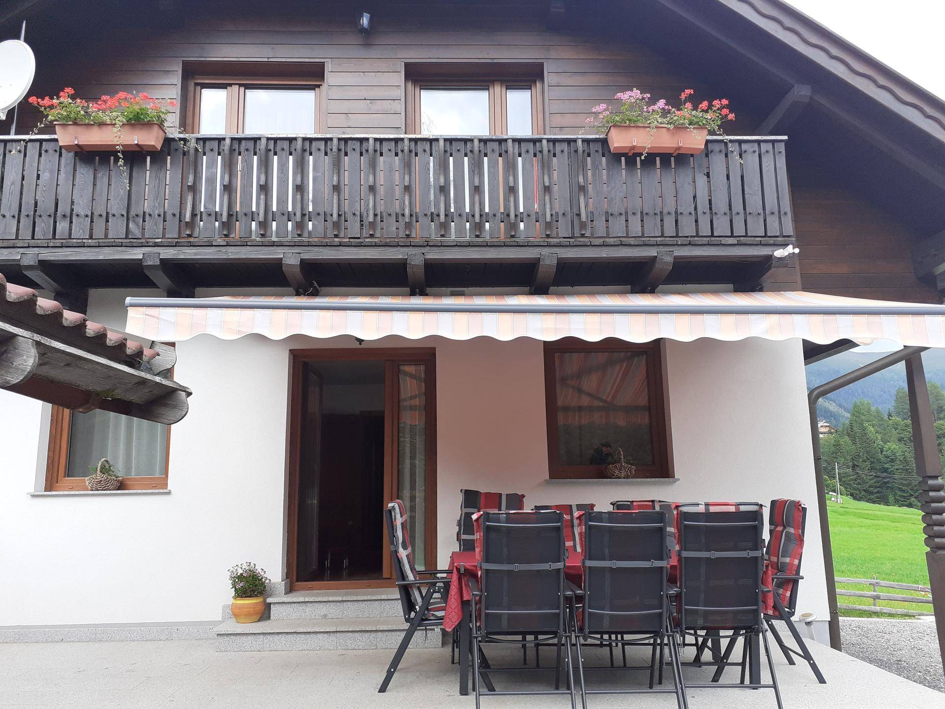 Gemütliche Terrasse mit Esstisch und Stühlen, geschützt durch eine Markise, mit Balkon darüber.