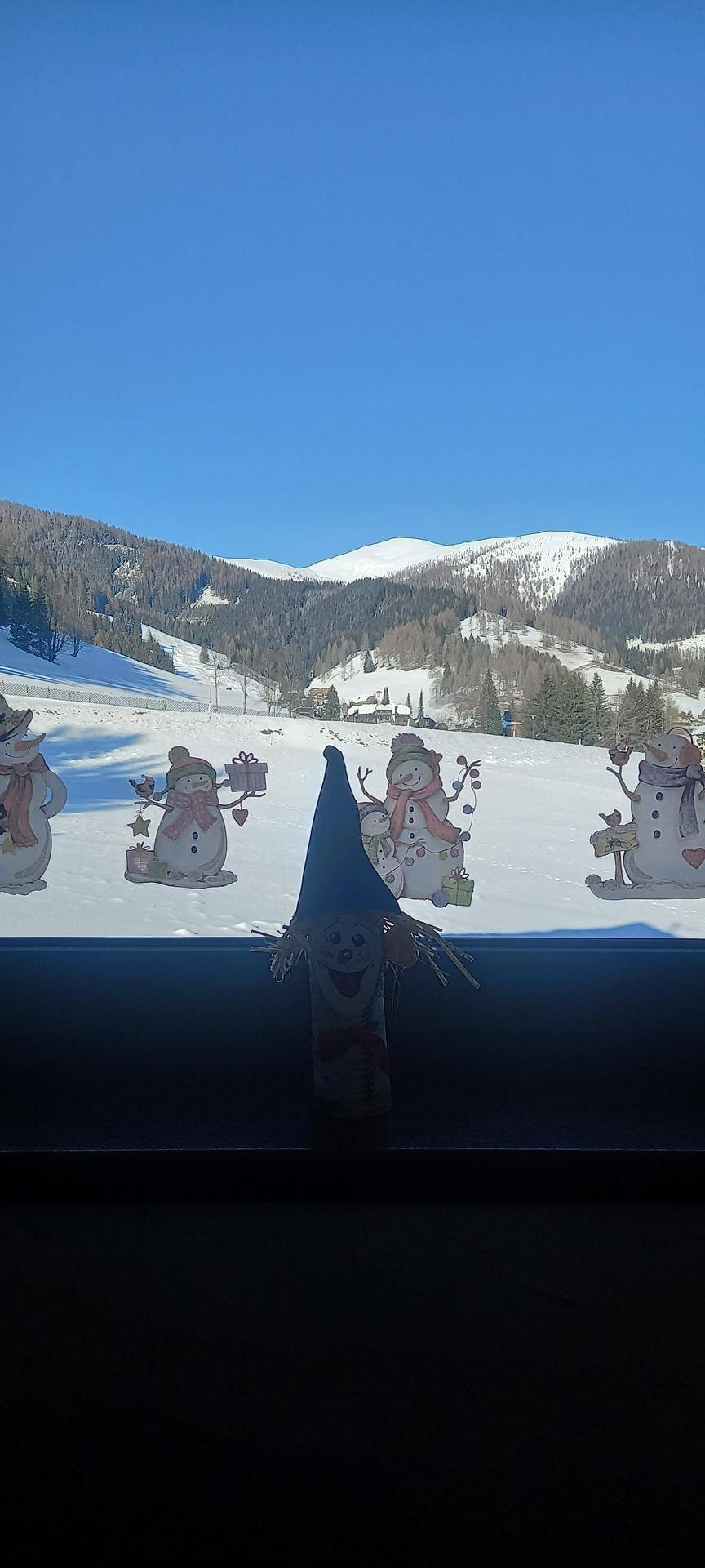 Winterliche Berglandschaft mit Schnee und blauem Himmel, gesehen durch ein Fenster.