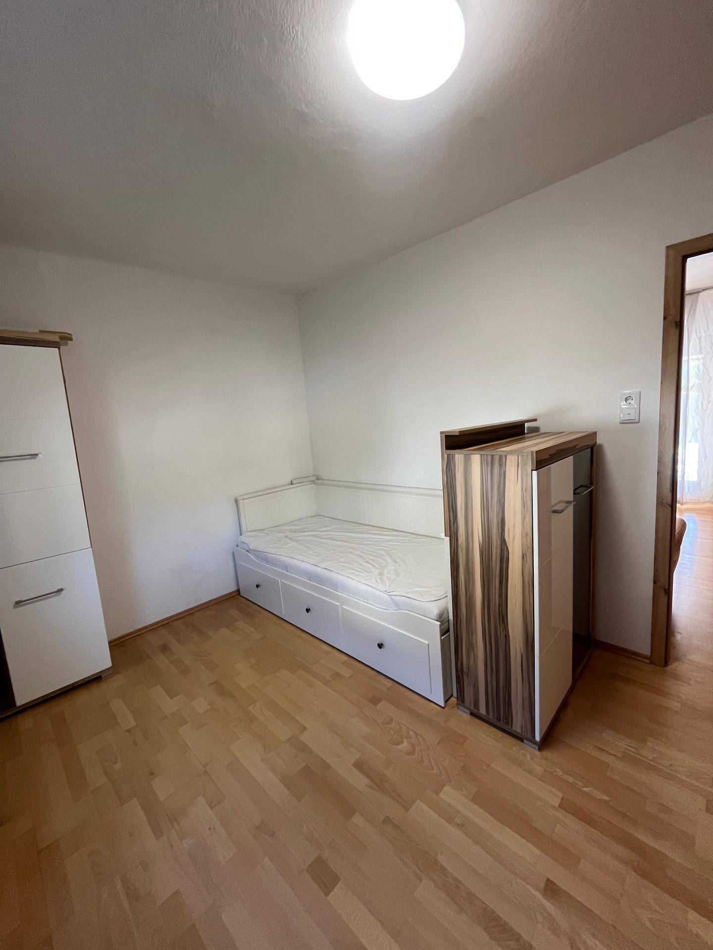 Helles Zimmer mit Einzelbett, Schrank und Holzoptik-Boden.