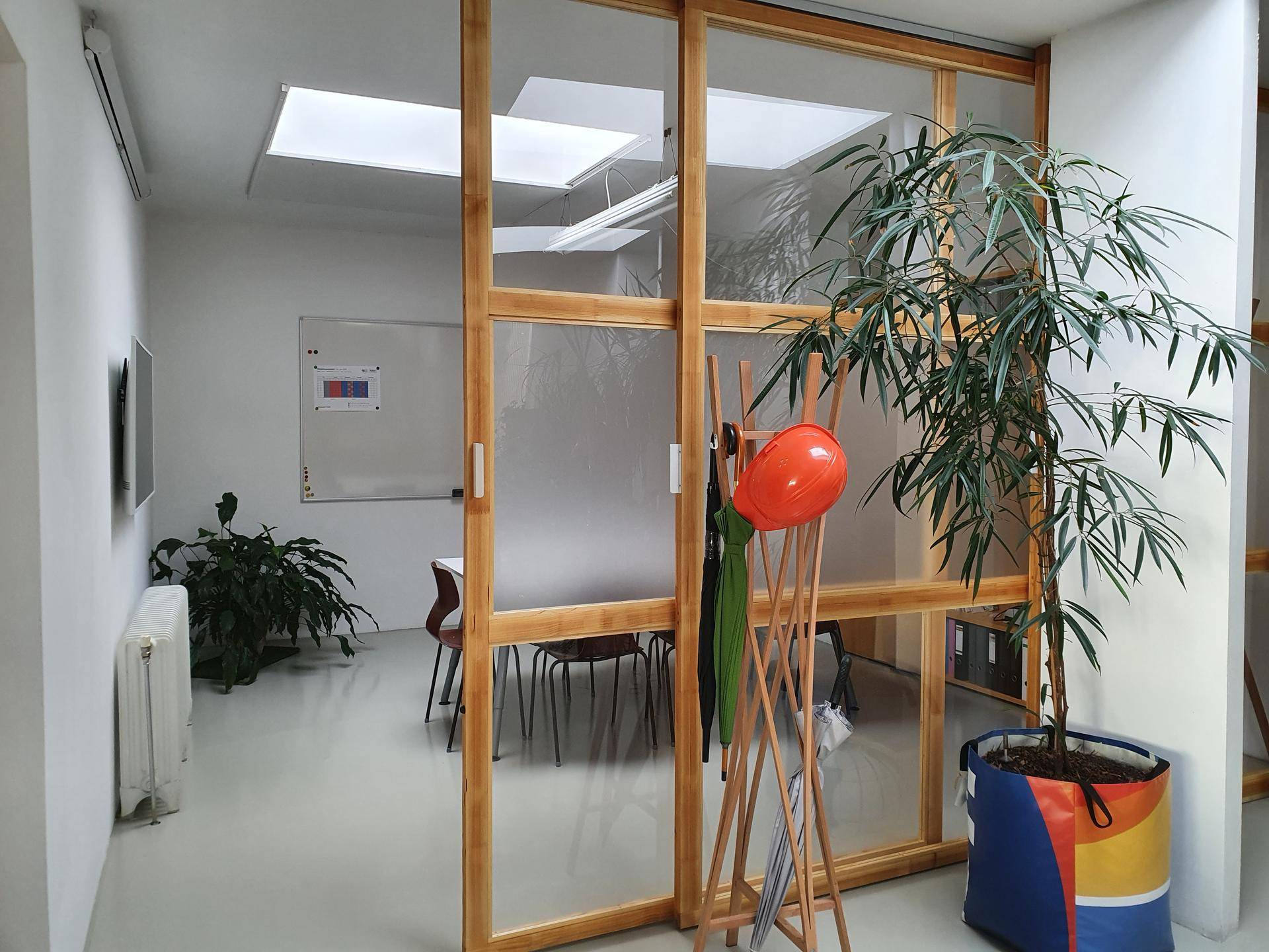 Heller Flurbereich mit großer Pflanze, Garderobe und einer Glaswand, die zu einem Besprechungsraum führt.