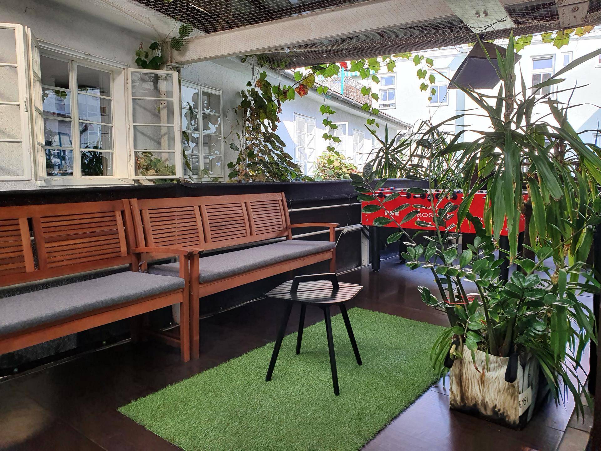 Gemütlicher überdachter Balkon mit Holzbänken, vielen Pflanzen und einem Tischkicker für Freizeitaktivitäten.