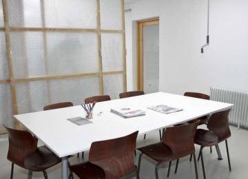 Heller Konferenzraum mit großem weißen Tisch, braunen Stühlen und einer transluzenten Trennwand.