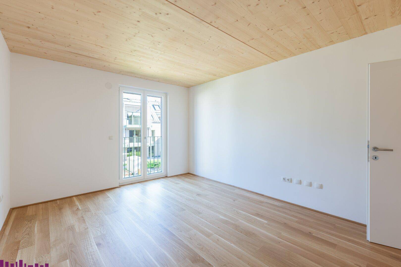 Helles Zimmer mit Holzboden und Holzdecke sowie Zugang zu einem französischen Balkon.