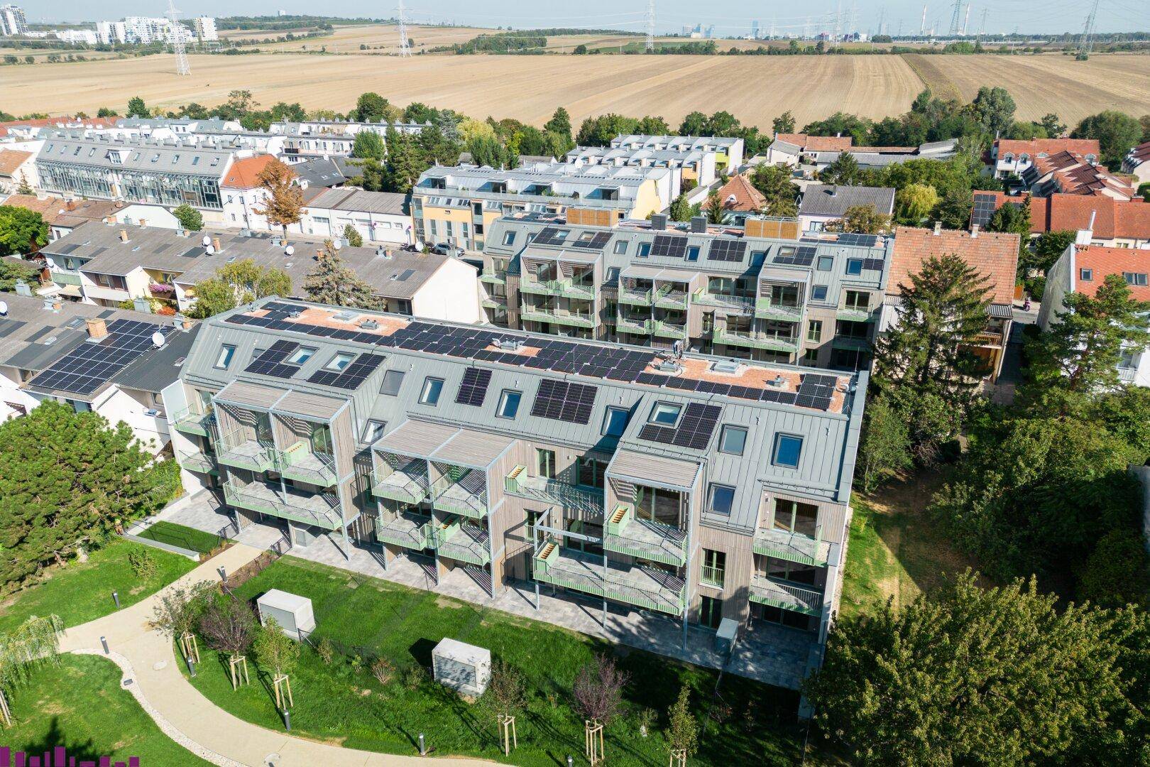 Luftaufnahme eines modernen Wohnkomplexes mit Solaranlagen auf den Dächern und umliegender Natur.