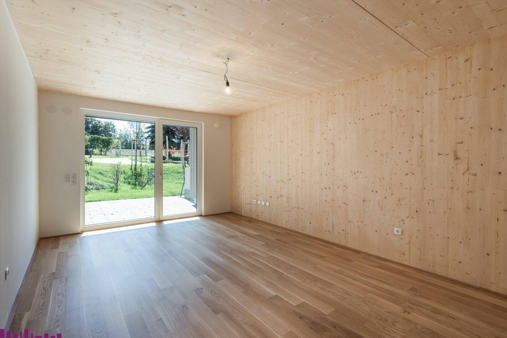 Heller Raum mit Holzwänden, Holzboden und einer großen Schiebetür mit Blick ins Grüne.