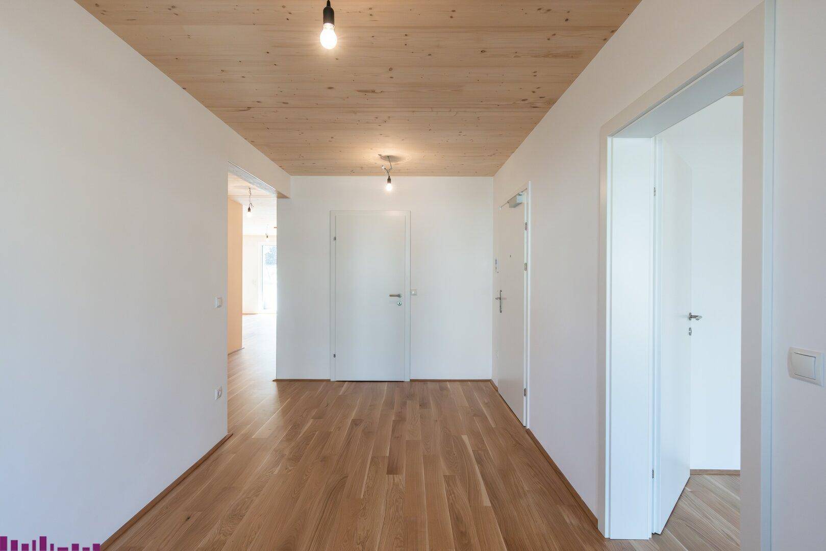 Heller Flur mit Holzboden, weißen Wänden und mehreren Türen, die zu anderen Räumen führen.