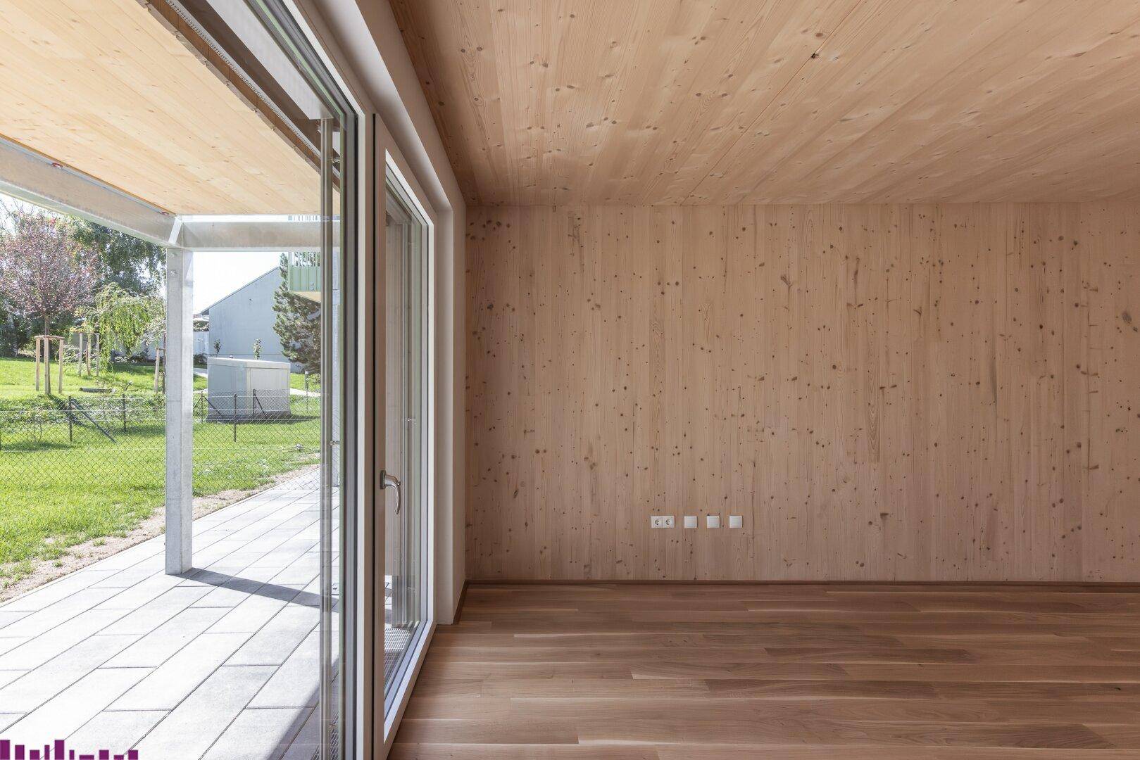 Leerer Raum mit Holzwänden, Holzboden und großen Schiebetüren, die zu einer Terrasse führen.