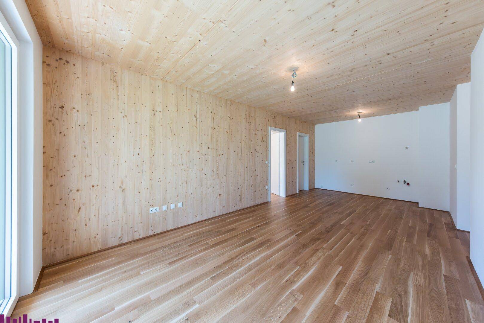 Unmöblierter Raum mit Holzwänden, Holzboden und einer einfachen Deckenbeleuchtung.