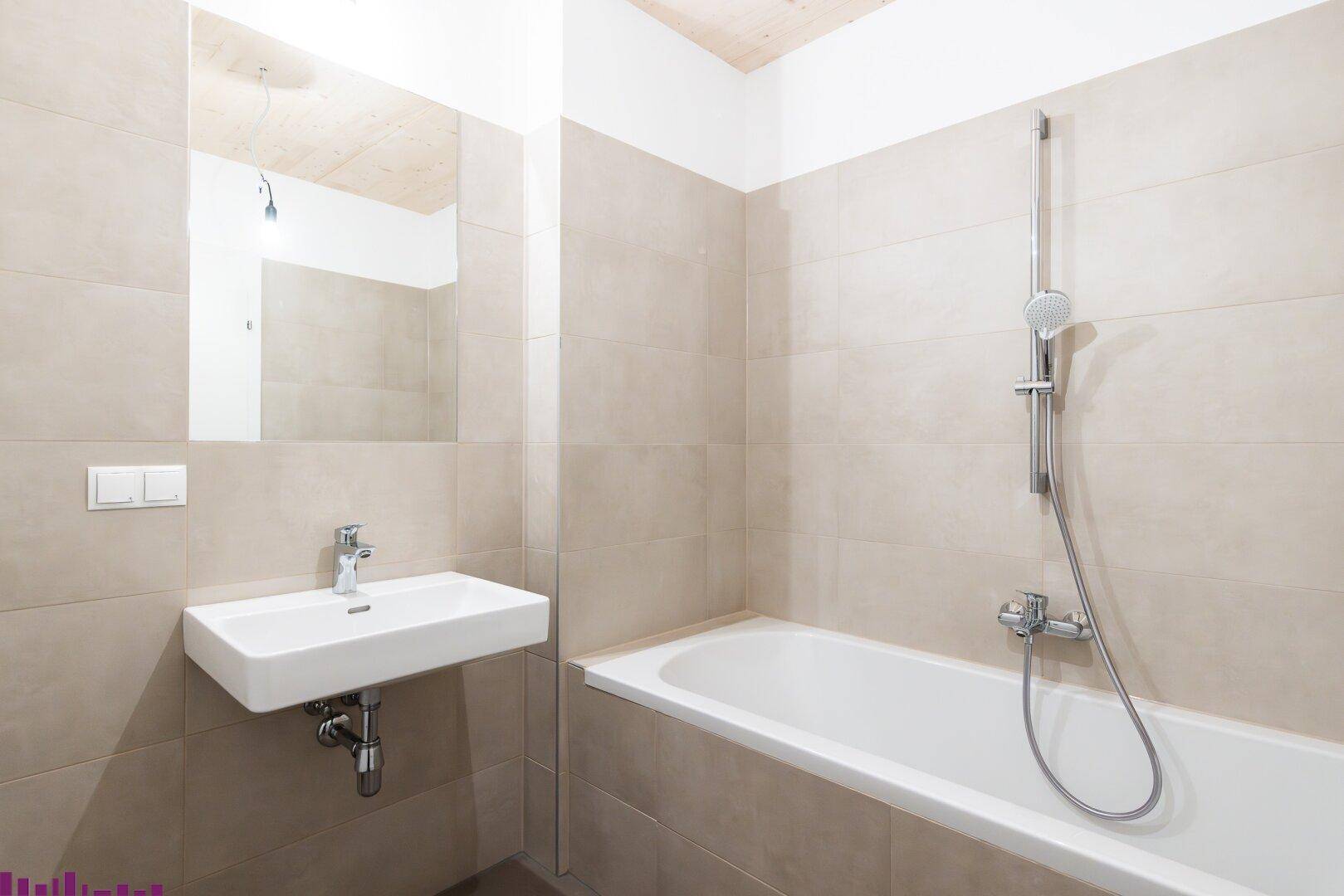 Modernes Badezimmer mit Badewanne, wandmontiertem Waschbecken und beigefarbenen Fliesen.