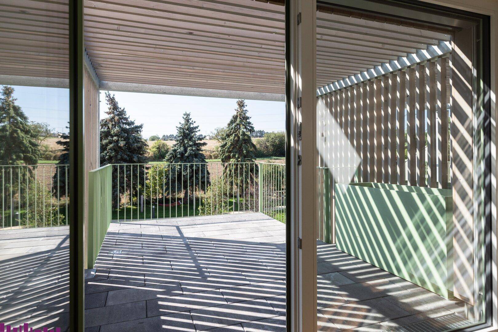 Geräumiger Balkon mit Fliesenboden, Holzverkleidung und weitem Blick ins Grüne.