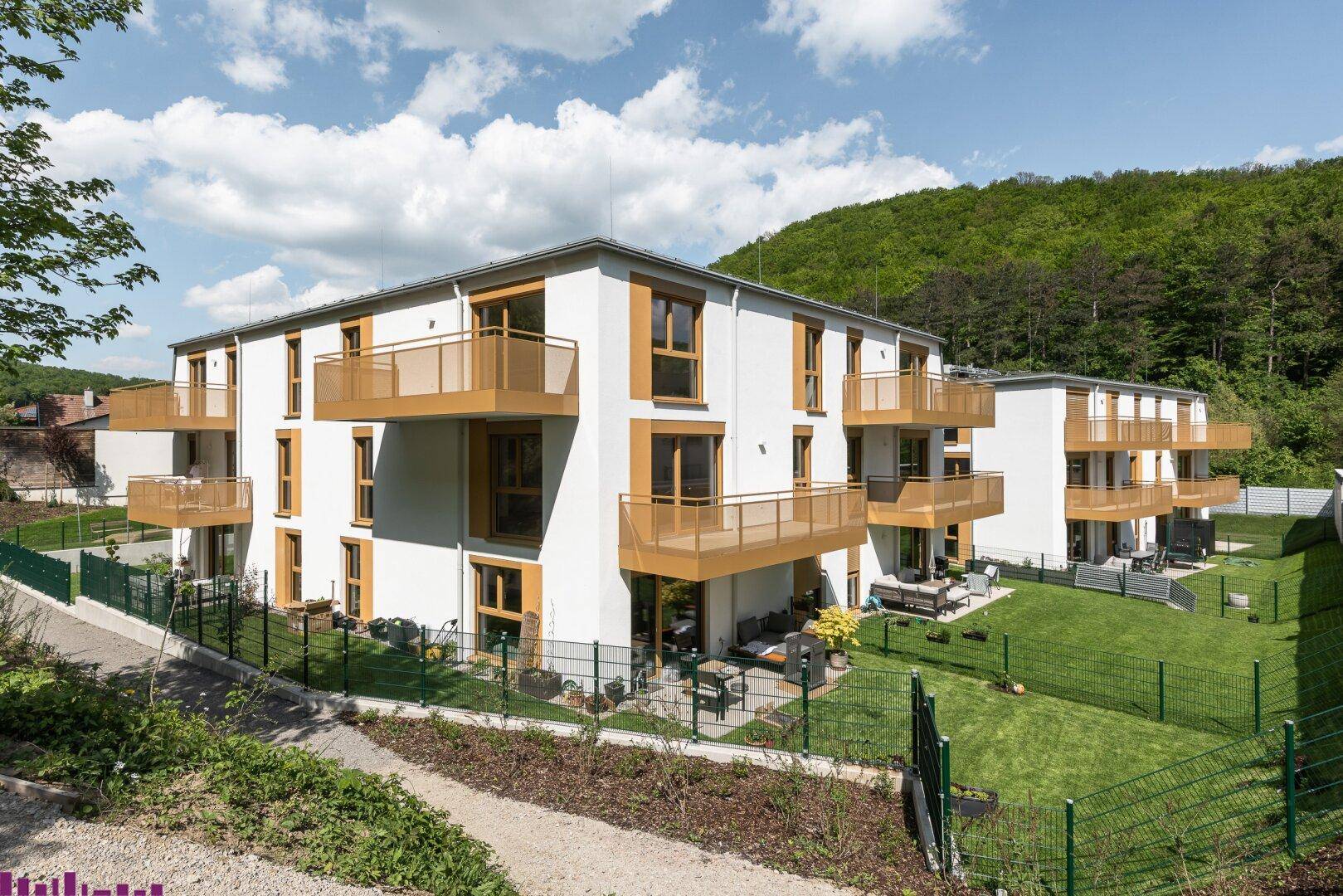 Moderne Wohngebäude mit hellen Fassaden, Balkonen und privaten Gärten in grüner Umgebung.