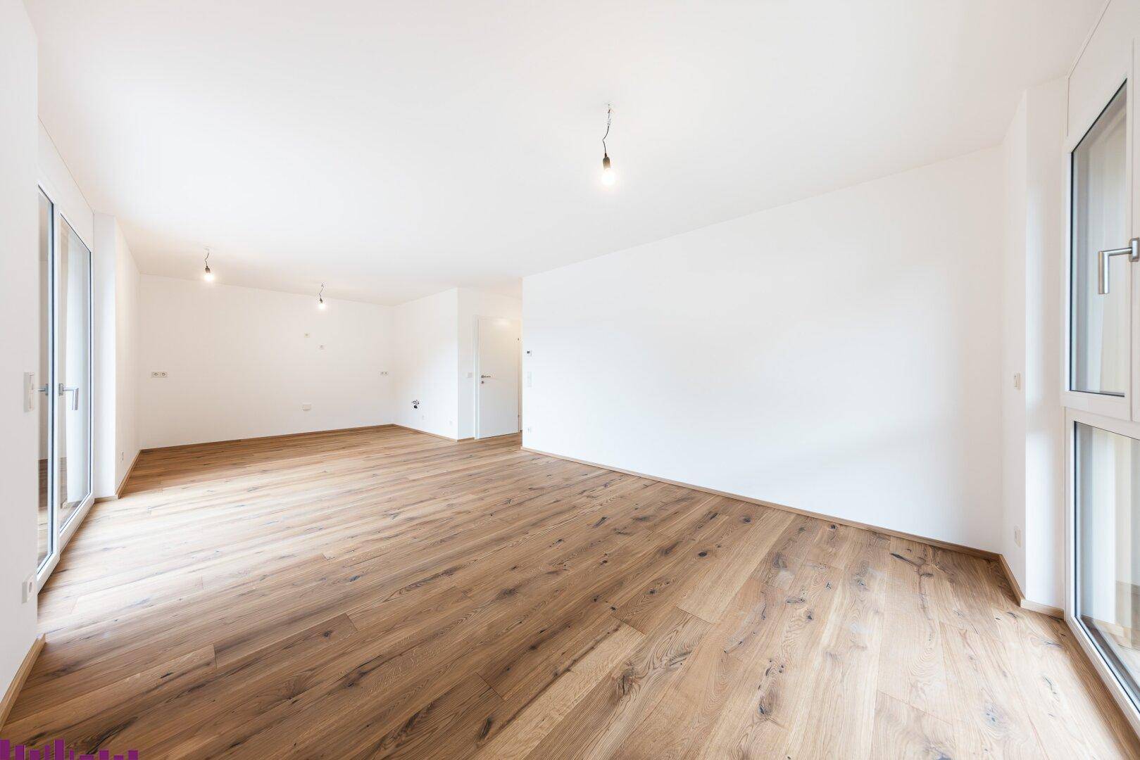 Helles, leeres Zimmer mit Holzboden und großen Fenstern, bereit für die individuelle Gestaltung.