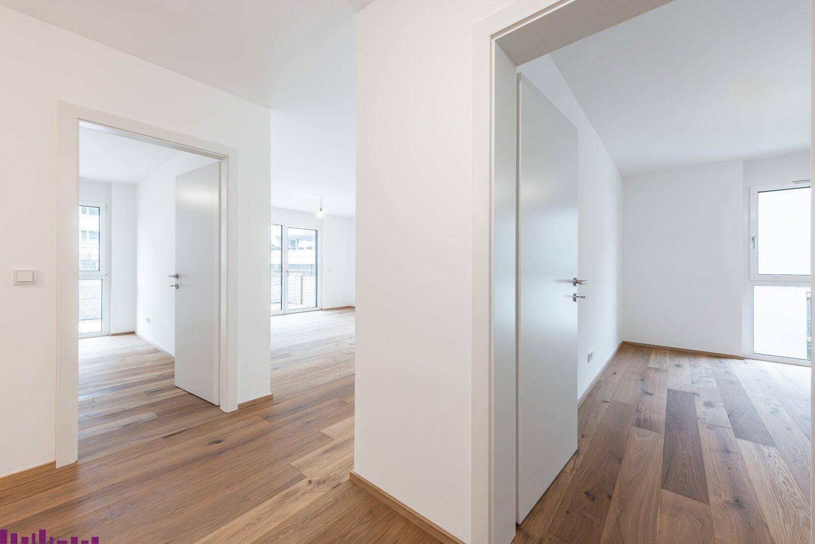 Heller Flur mit Holzboden und weißen Türen, der zu weiteren Räumen führt.