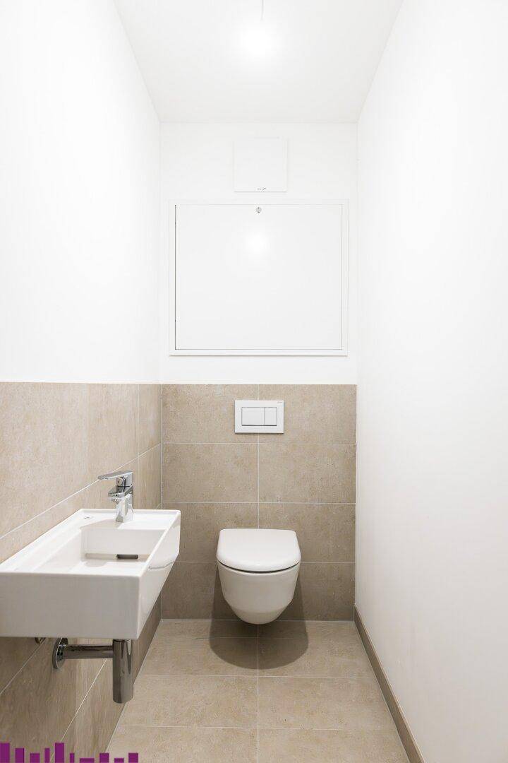Modernes Gäste-WC mit wandhängendem WC, kleinem Waschbecken und beigen Fliesen.