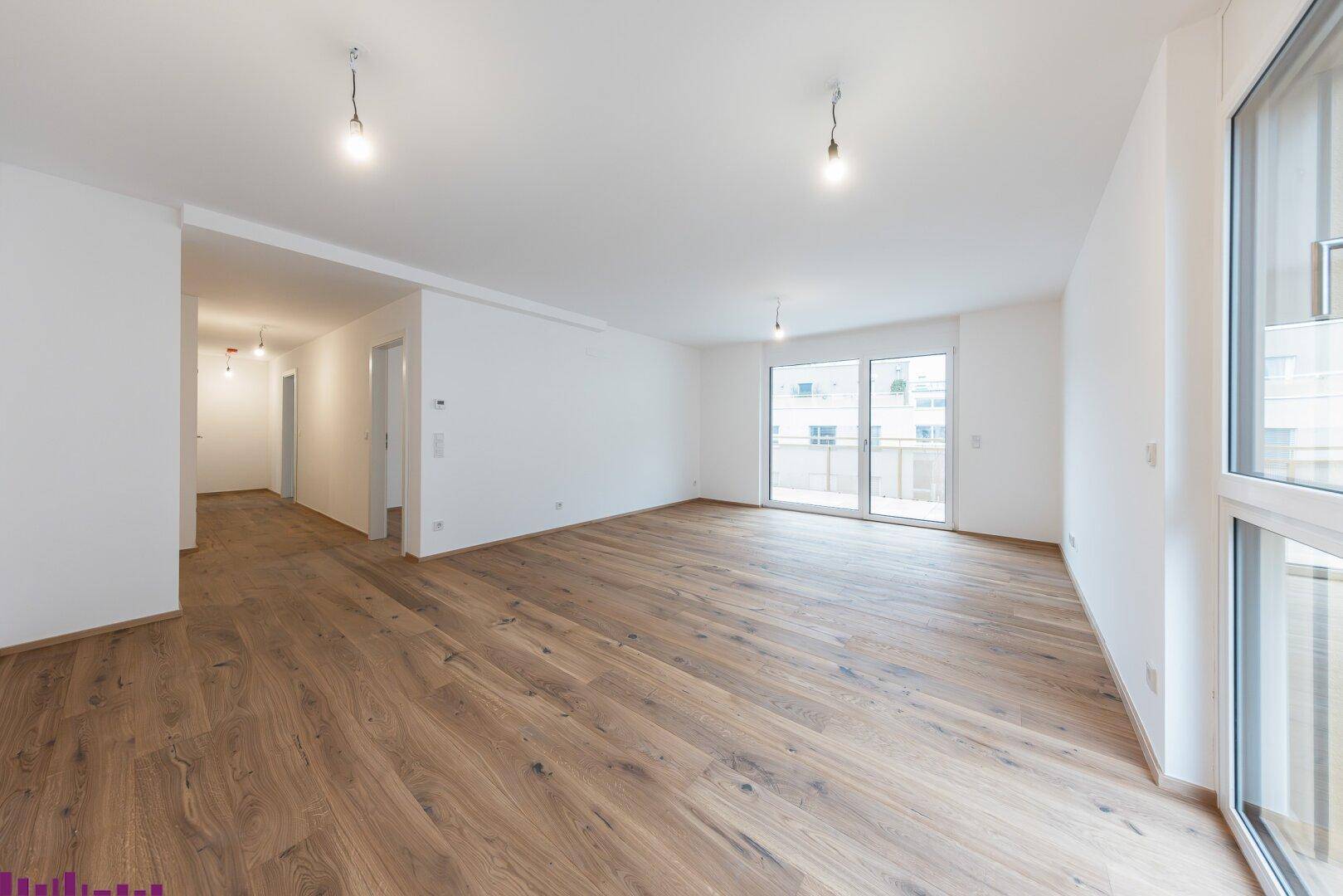 Geräumiger Wohnbereich mit Holzboden, viel Tageslicht und Blick zum Flur und Balkon.