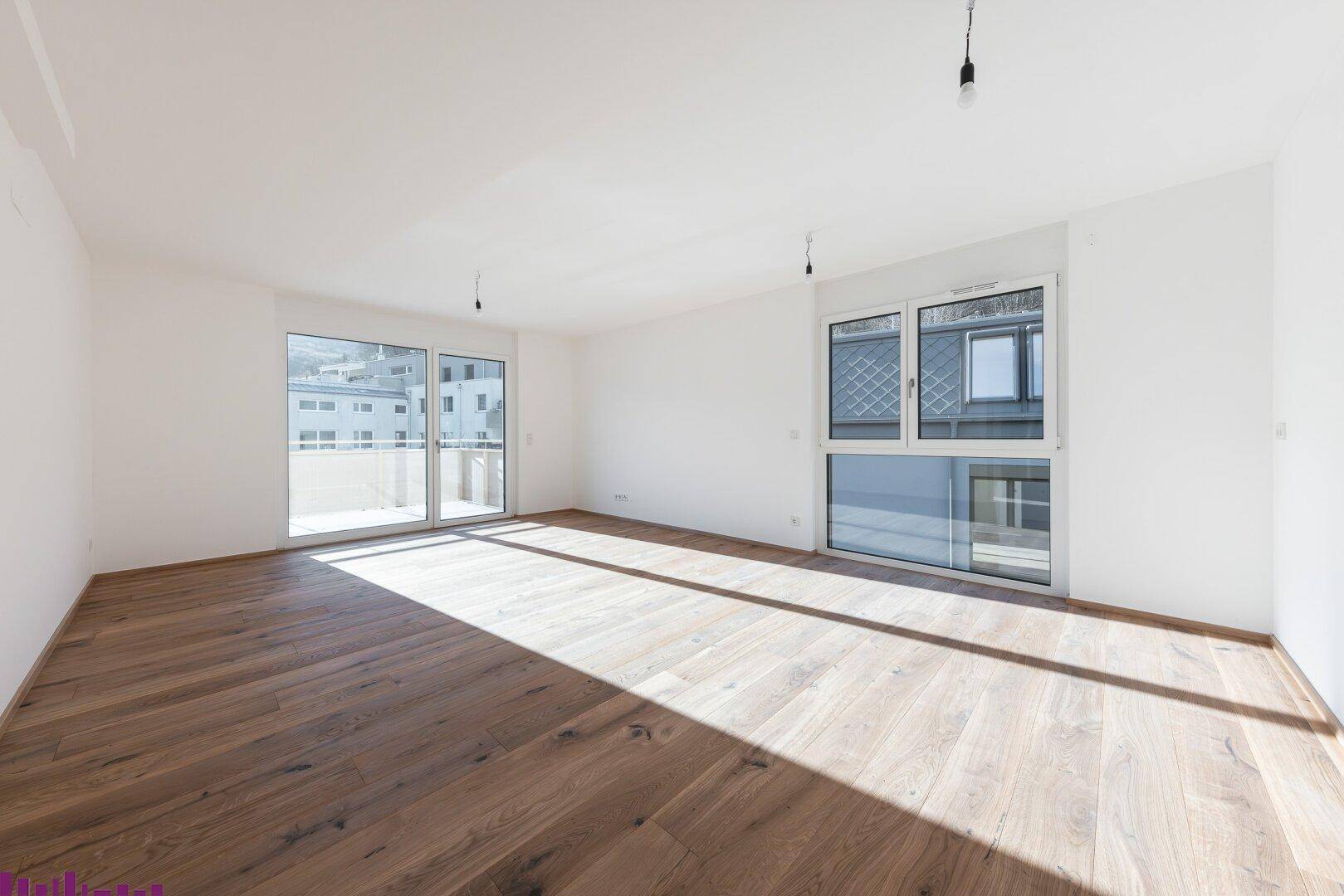 Helles Wohnzimmer mit Holzboden, großen Fenstern und Zugang zum Balkon.