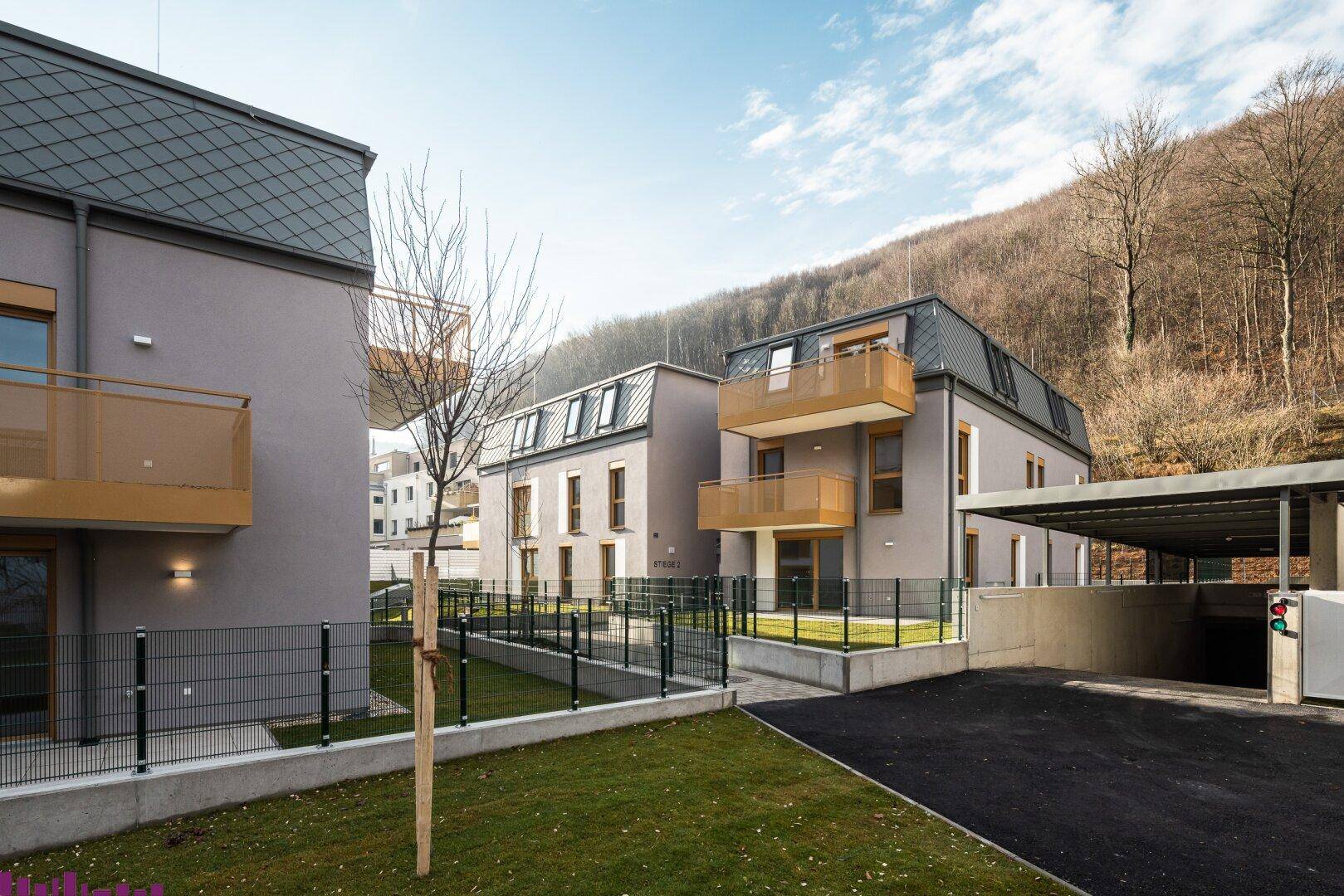 Wohngebäude mit Mansarddach, Balkonen und Carport in einer ruhigen, grünen Umgebung.