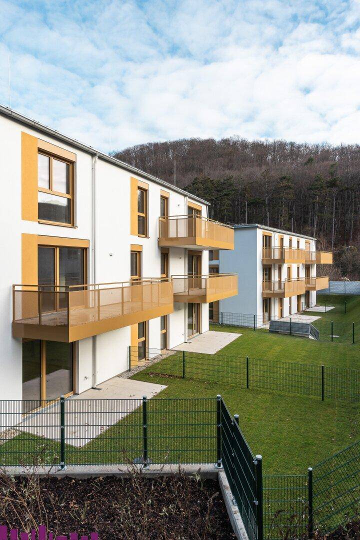 Moderne Wohngebäude mit Balkonen und Terrassen, umgeben von grünen Hügeln.