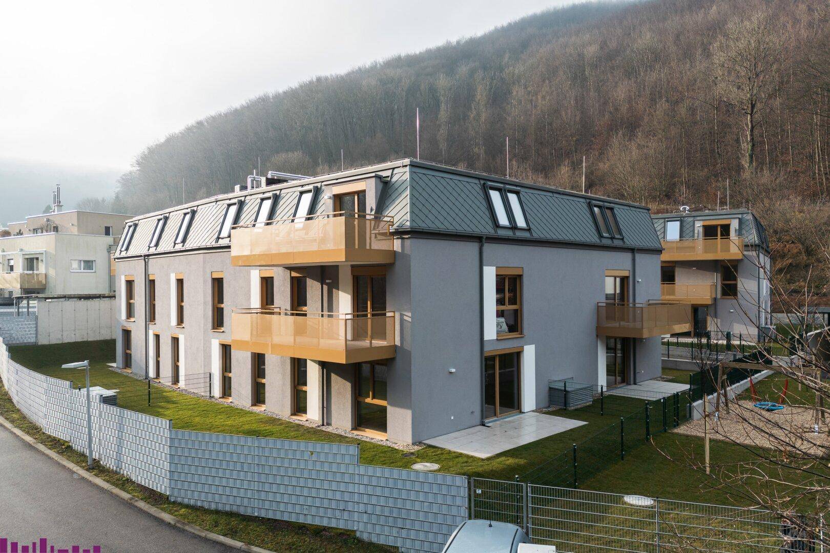 Wohnanlage mit Mansarddächern, Balkonen und Terrassen in einer naturnahen Umgebung.