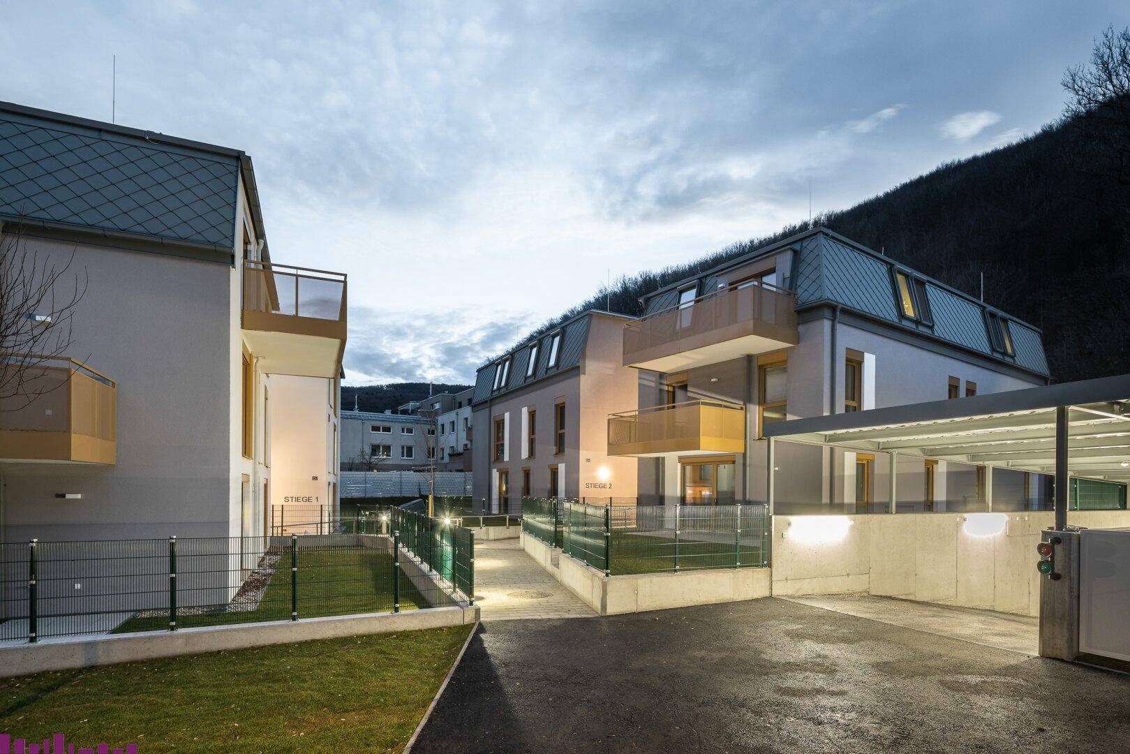 Wohnanlage bei Dämmerung mit beleuchteten Außenbereichen und Carport.