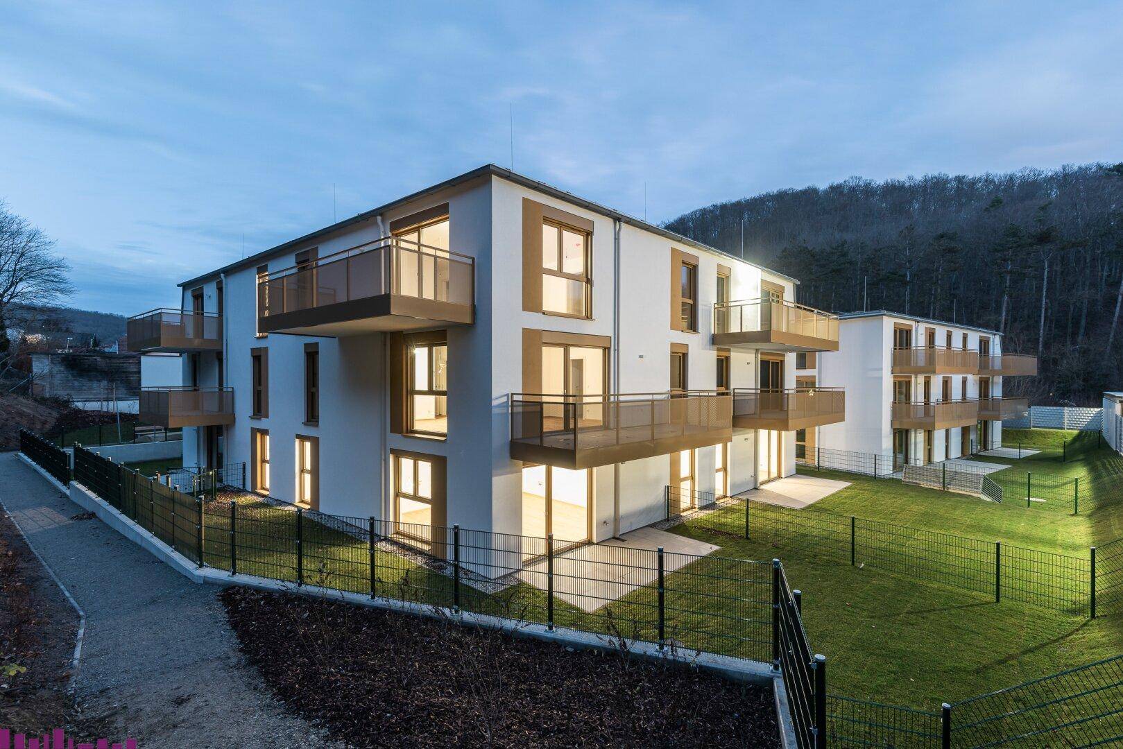 Moderne Wohngebäude bei Abenddämmerung mit beleuchteten Balkonen und Terrassen.