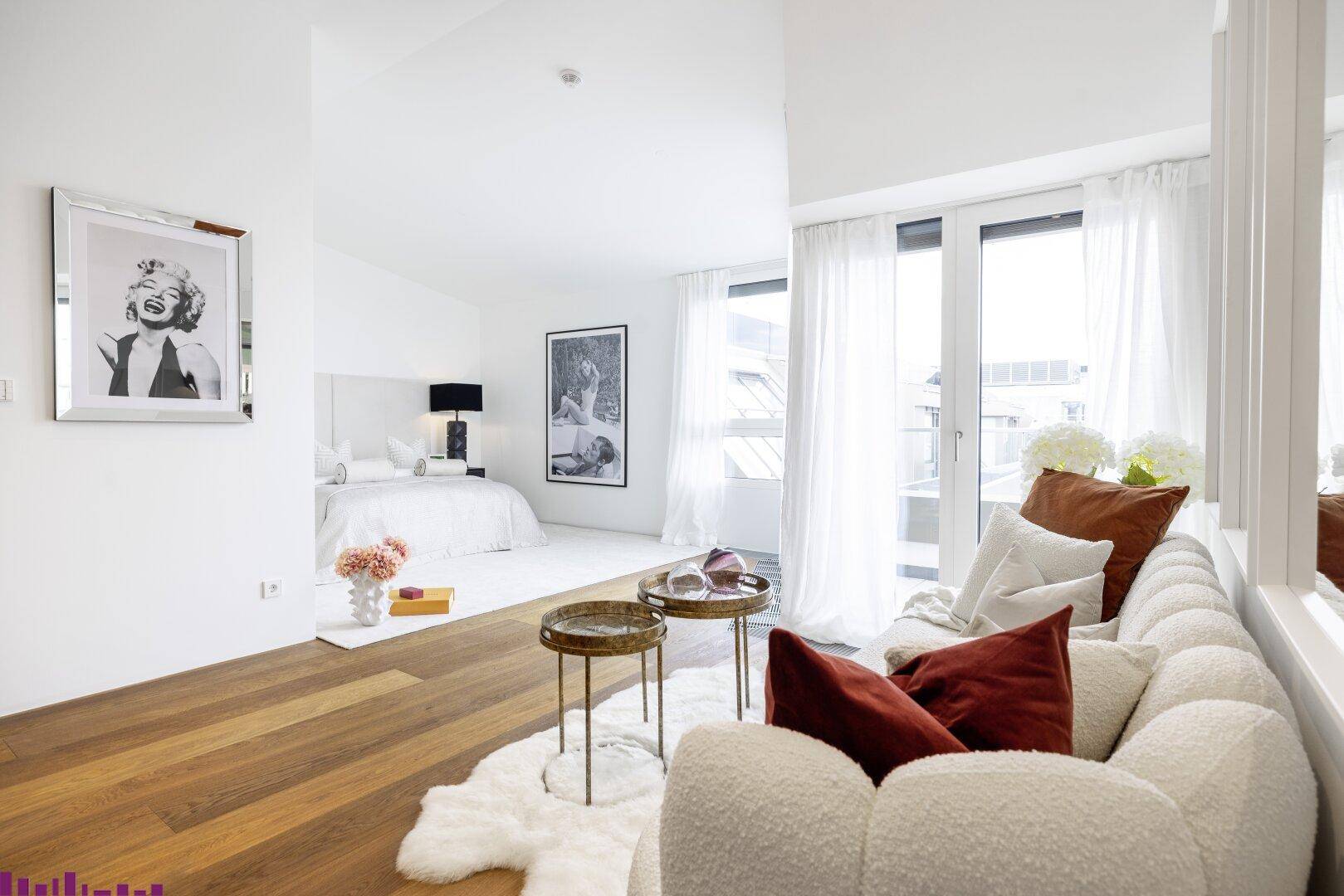 Helles Schlafzimmer mit Holzboden, großen Fenstern und modernem, offenem Wohnbereich in Weißtönen.