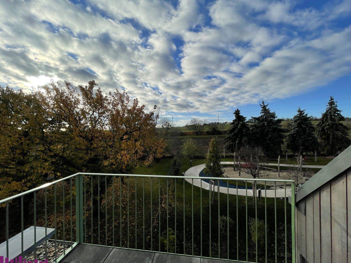 Balkon mit Holzboden und weitem Blick über die Landschaft und den Spielplatz.