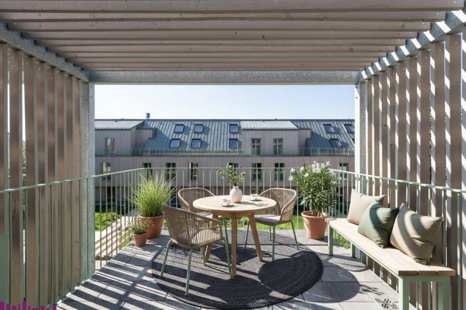 Möblierter Balkon mit Holzelementen und Blick auf die gegenüberliegende Wohnanlage.