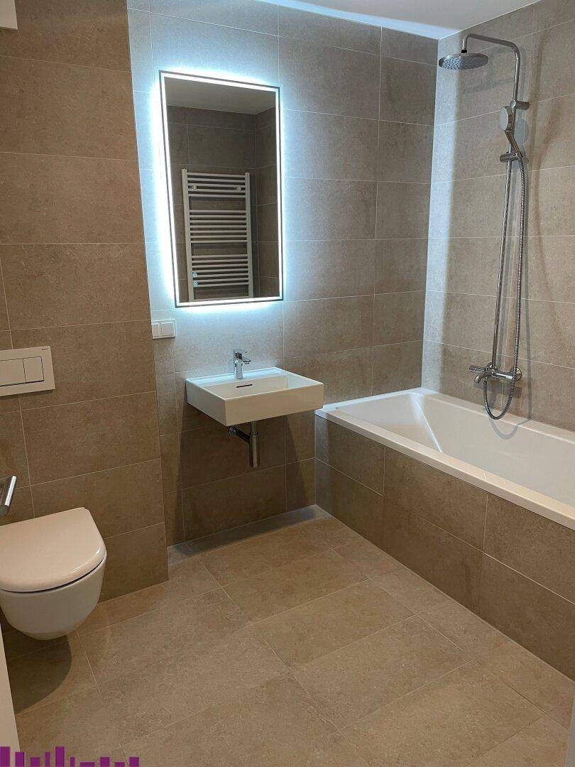 Modernes Badezimmer mit Badewanne, Dusche und beleuchtetem Spiegel über dem Waschbecken.
