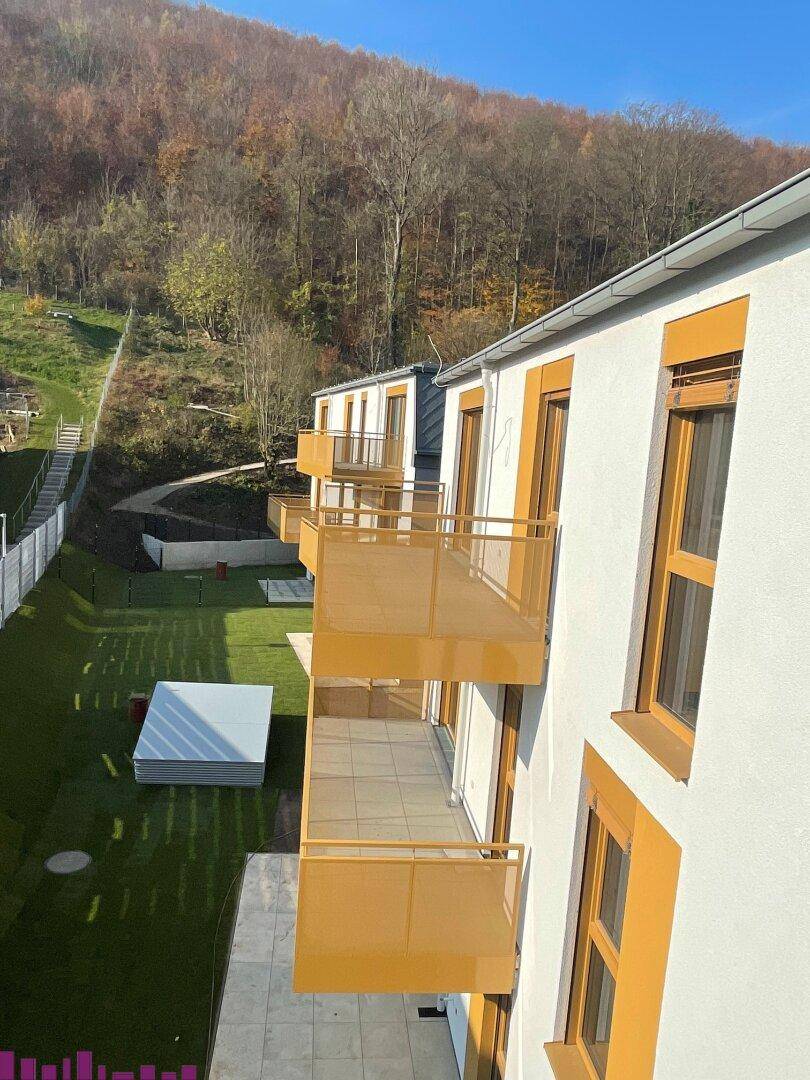 Seitenansicht eines modernen Wohngebäudes mit mehreren Balkonen und Grünflächen.