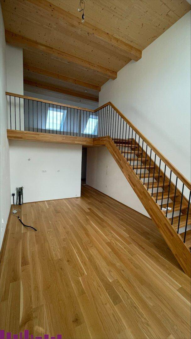 Geräumiger Flurbereich mit Holztreppe, Galerie und hohen Decken, der verschiedene Ebenen verbindet.