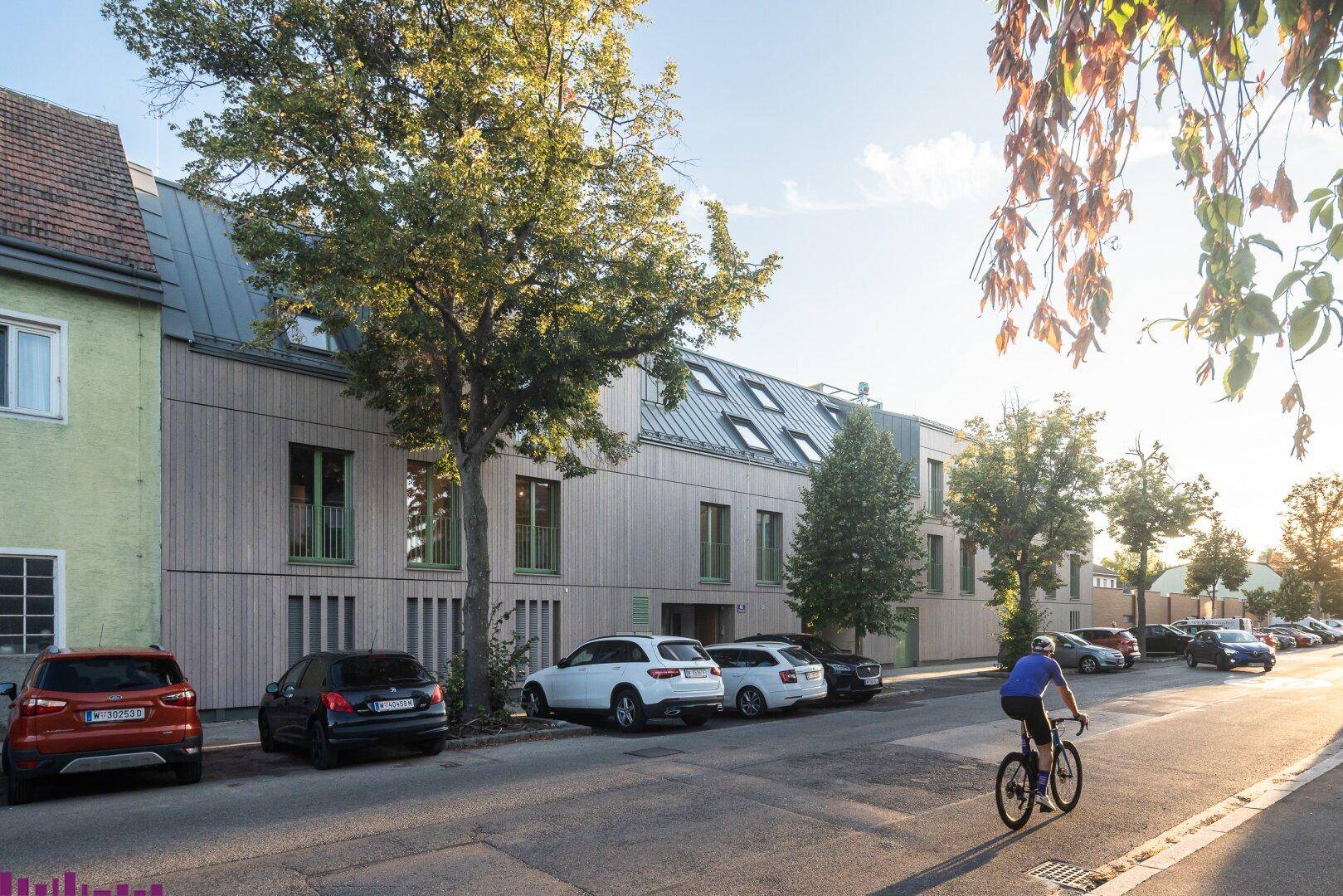 Moderne Wohnanlage mit Holzfassade und begrüntem Umfeld an einer ruhigen Straße.