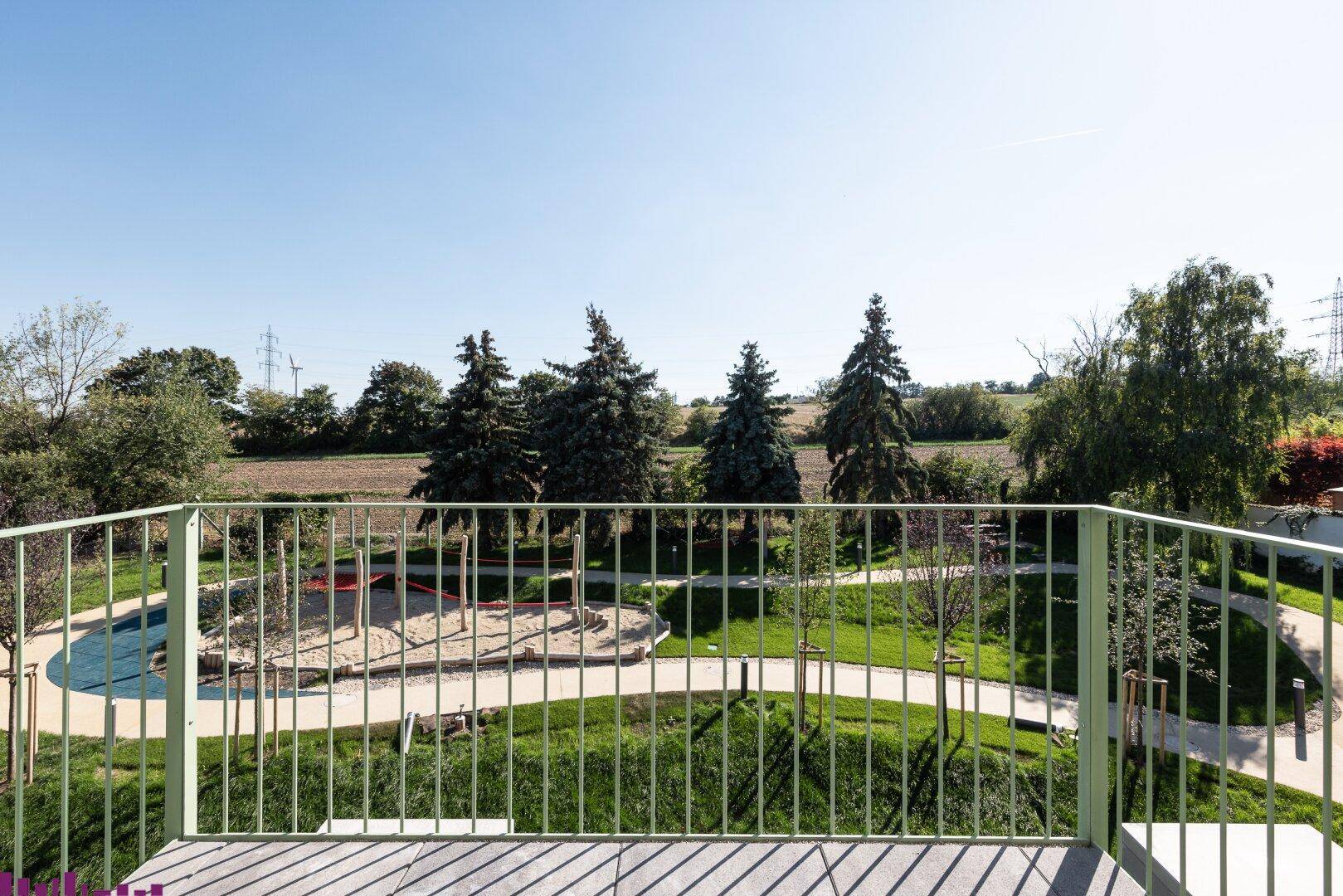 Geräumiger Balkon mit weitem Blick über einen grünen Spielplatz und die ländliche Umgebung.