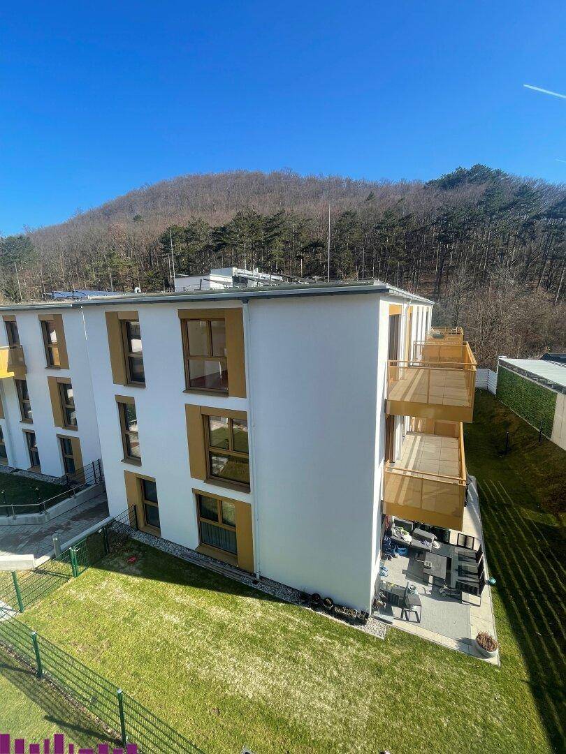 Moderne Wohnanlage mit weißen Fassaden, Balkonen und Blick auf bewaldete Hügel.
