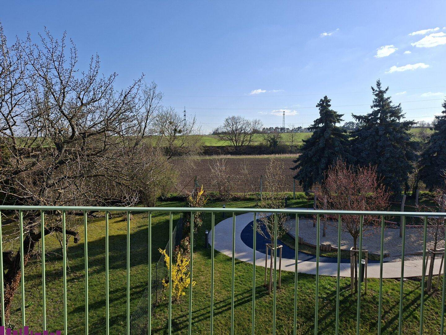 Weitläufiger Blick über grüne Felder und Bäume von einem Balkon oder einer Terrasse.