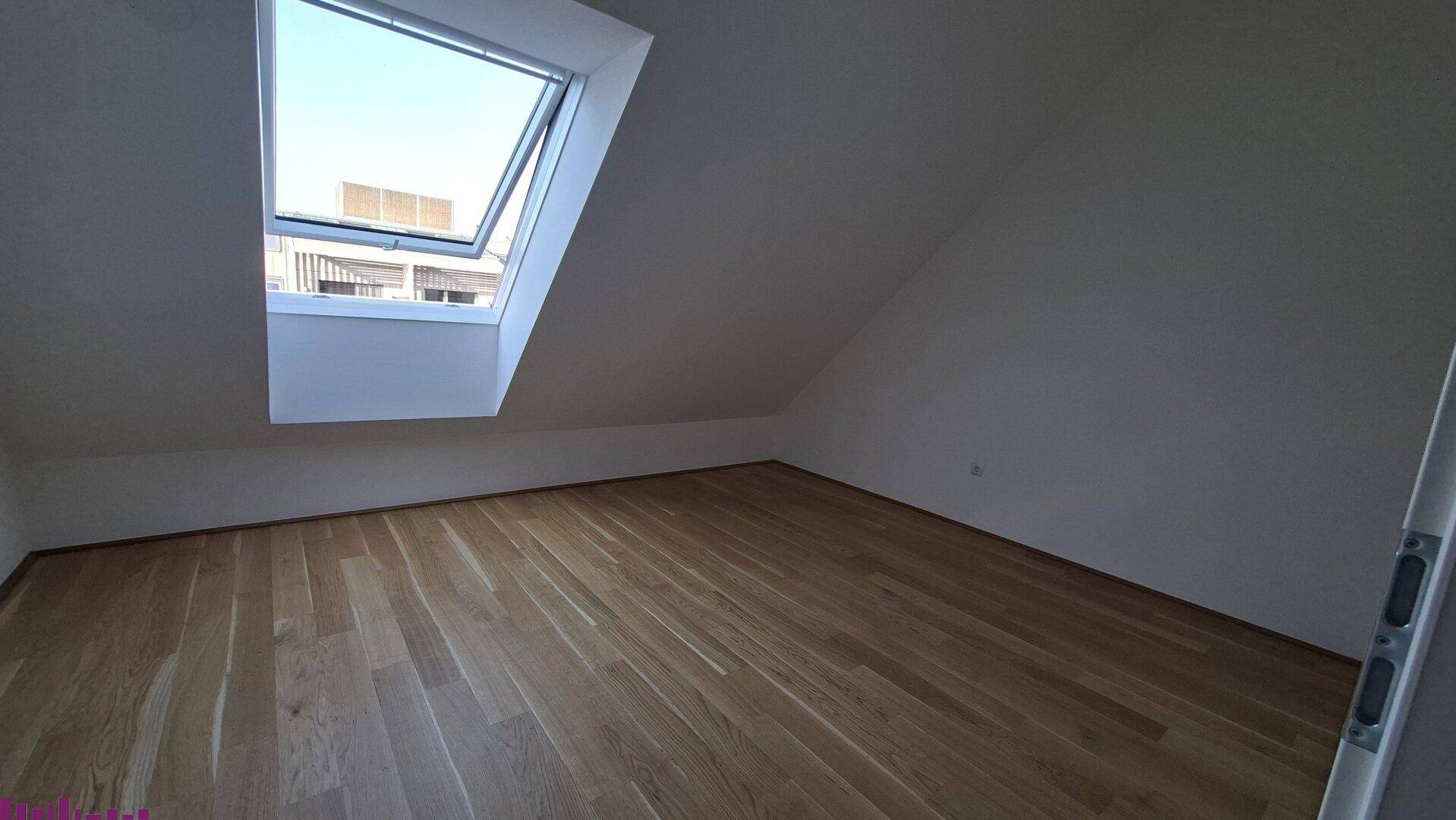 Leeres Zimmer im Dachgeschoss mit Holzboden und großem Dachfenster, ideal als Schlafzimmer.