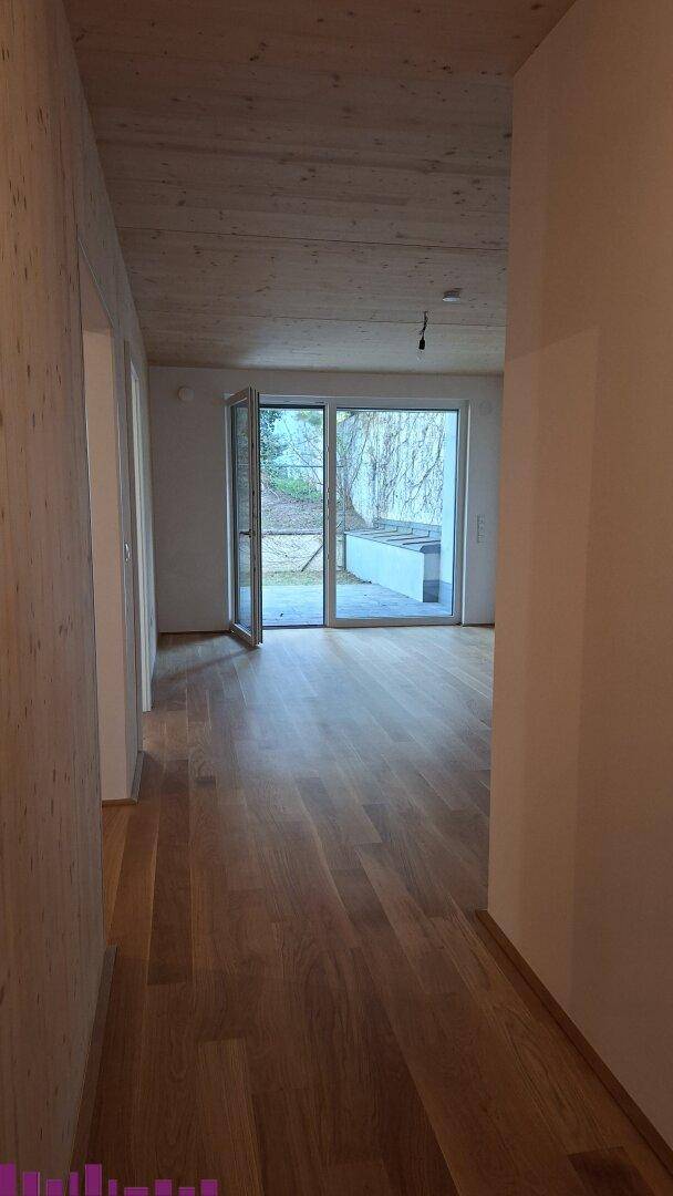 Heller Flur mit Holzboden und Blick in einen weiteren Raum mit großen Fenstern und Gartenzugang.