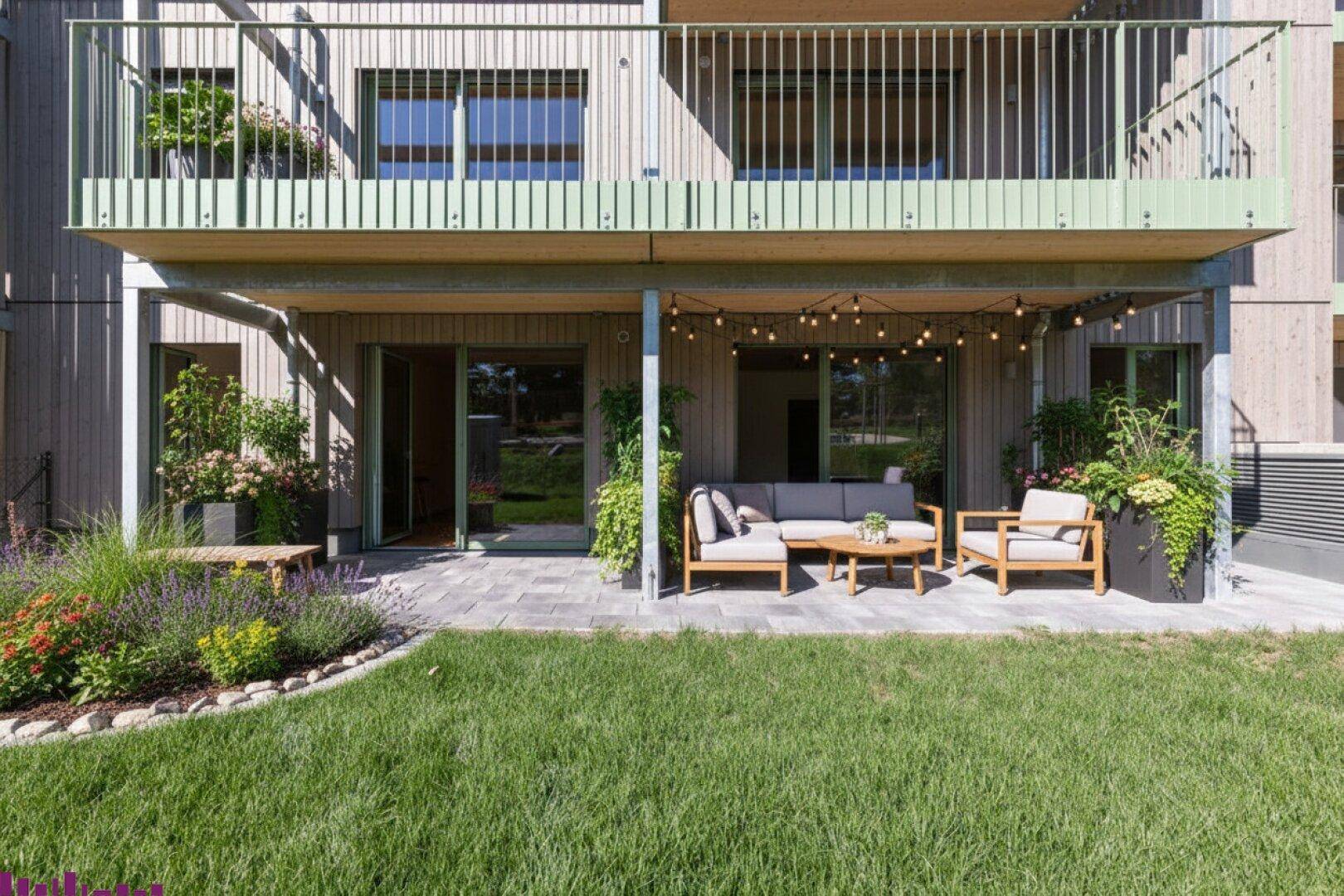 Gemütliche Terrasse mit modernen Gartenmöbeln, umgeben von gepflegten Grünflächen und Pflanzen unter einem Balkon.