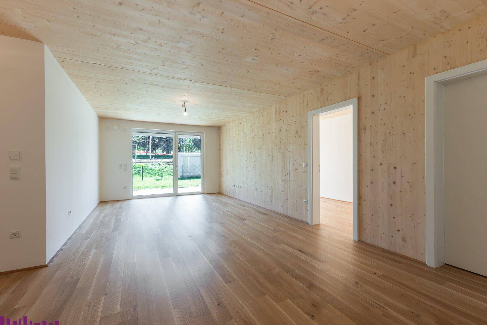 Heller Wohnraum mit Holzböden und Holzdecken, großen Schiebetüren zum Garten und viel natürlichem Licht.