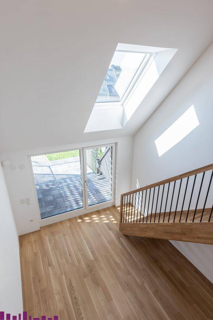 Heller Treppenaufgang mit Holzboden, großem Dachfenster und Zugang zur Terrasse.