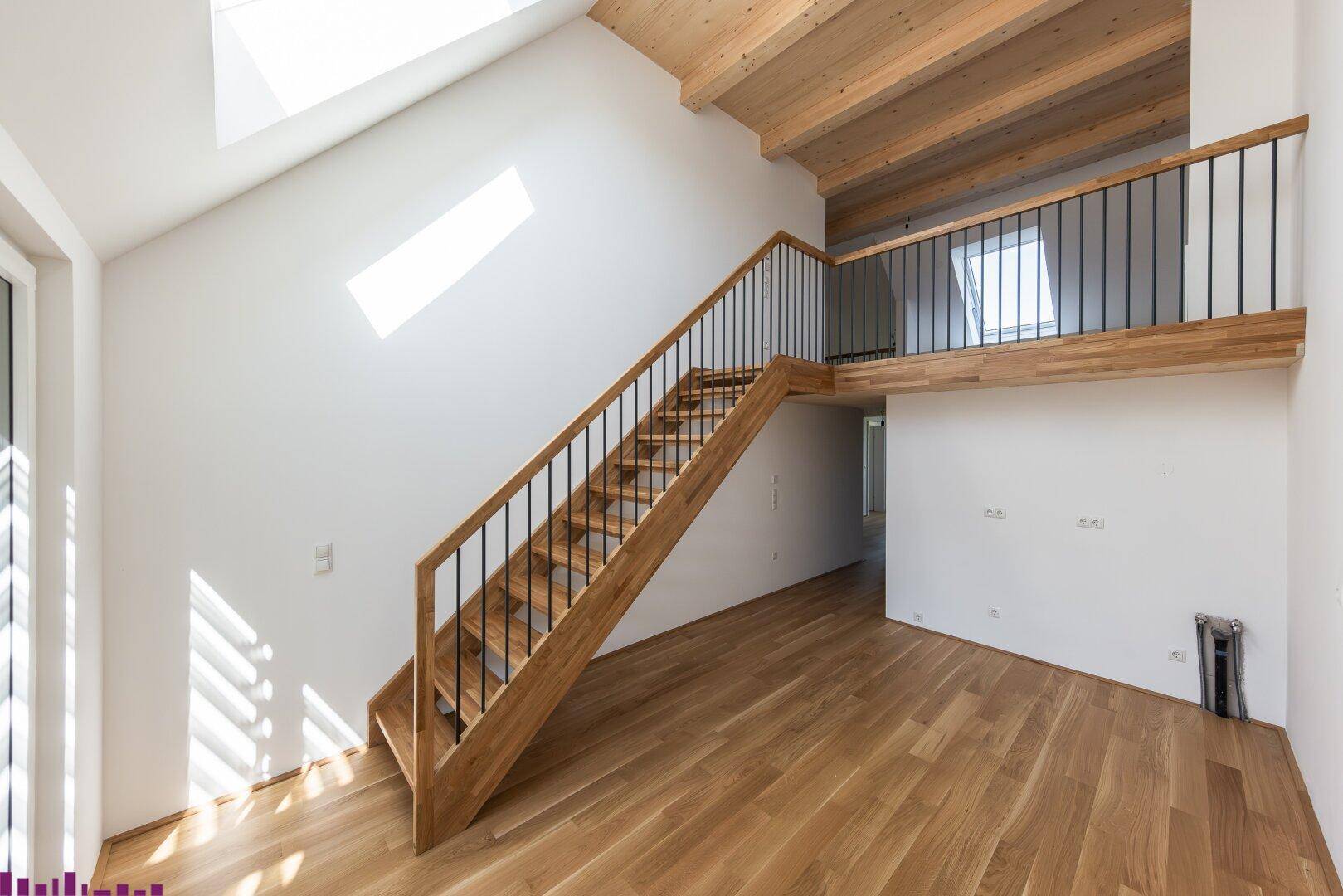 Geräumiger offener Wohnbereich mit Holztreppe, Galerie und sichtbaren Deckenbalken.