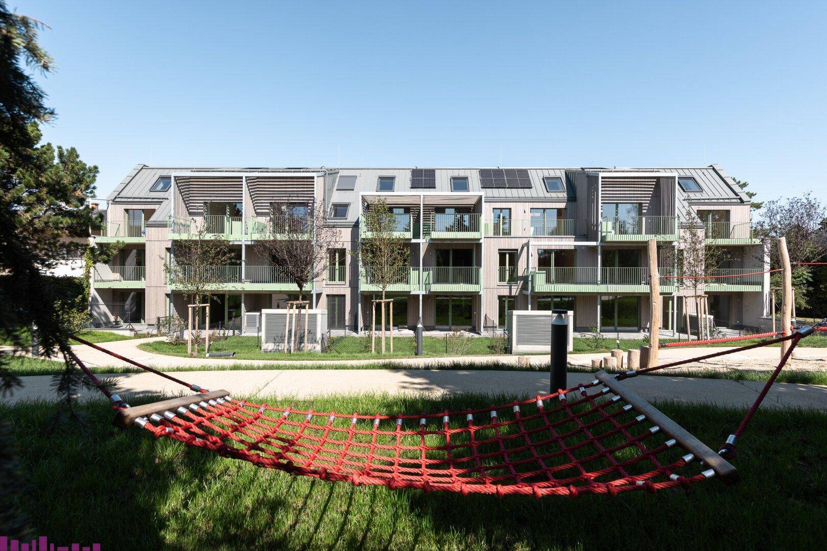 Moderne Wohnanlage mit Balkonen, Solarpaneelen auf dem Dach und einem Hängemattenbereich im Grünen.