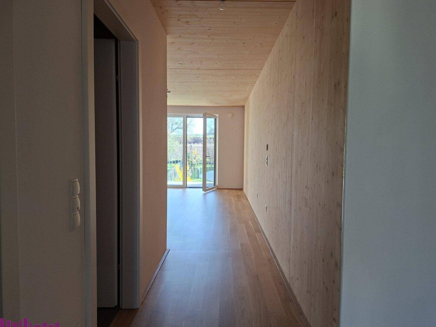 Heller Flur mit Holzboden und Holzdecke, der zu einem weiteren Raum führt.