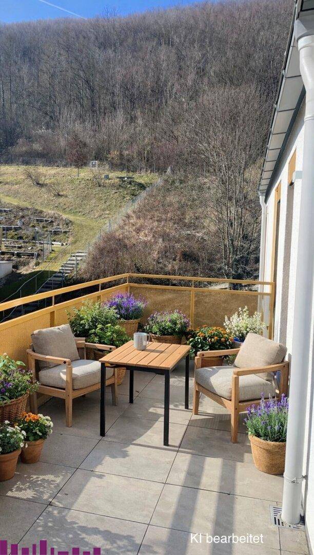 Heller Balkon mit bequemen Gartenmöbeln und vielen Pflanzen, ideal zum Entspannen mit Waldblick.